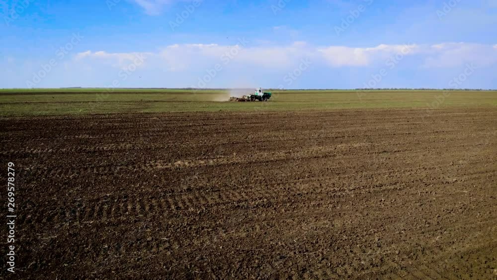 Overgrown with weeds field with tractor and cultivator under blue sky. Spring agricultural activities with heavy machinery Overgrown with weeds field with tractor and cultivator under blue sky. Spring agricultural activities with heavy machinery