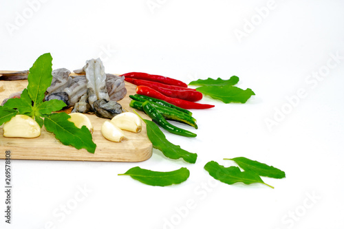 Many shrimp on a wooden chopping board around fresh chilies and basil leaves