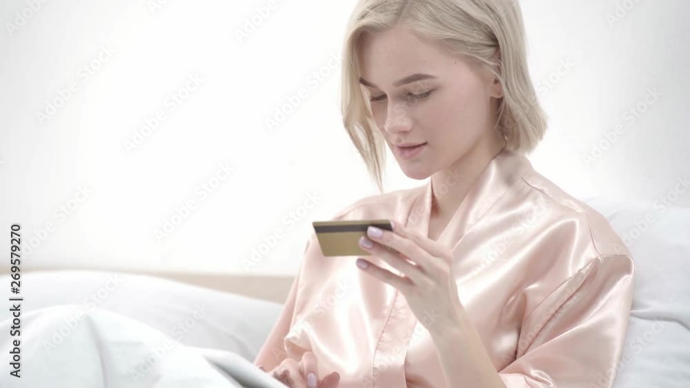 cheerful blonde girl holding digital tablet, taking credit card and smiling while online shopping in bed cheerful blonde girl holding digital tablet, taking credit card and smiling while online shopping in bed