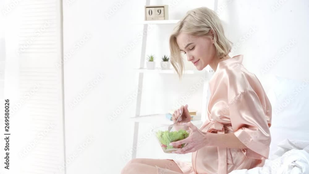 cheerful pregnant woman eating cherry tomato and touching belly while smiling in bedroom cheerful pregnant woman eating cherry tomato and touching belly while smiling in bedroom