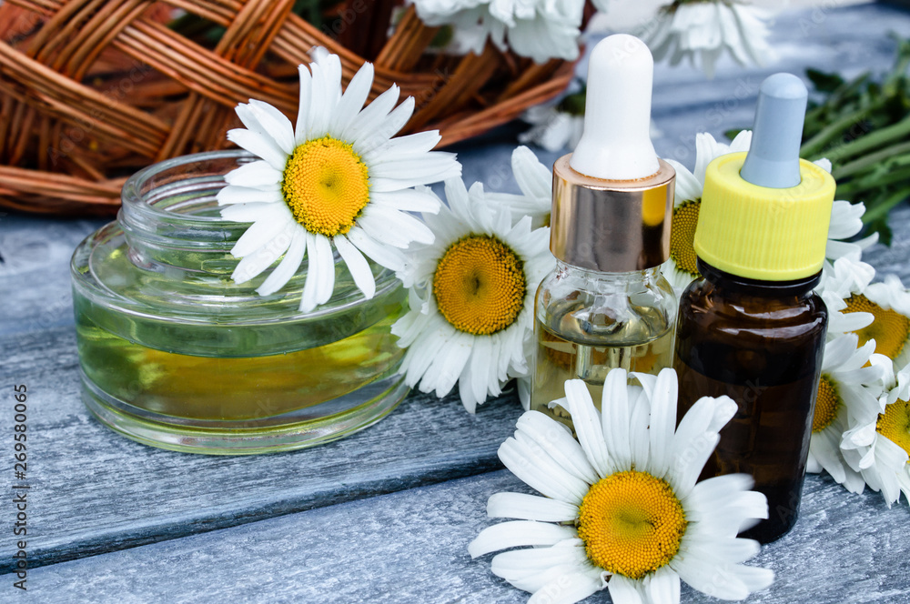 Chamomile essential oil in a glass jar and a bottle near chamomile.
