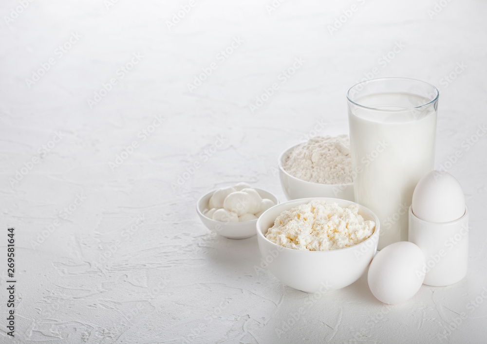 Fresh dairy products on white table background. Glass of milk, bowl of baking flour, cottage cheese and mozzarella. Eggs and cheese. Space for text Fresh dairy products on white table background. Glass of milk, bowl of baking flour, cottage cheese and mozzarella. Eggs and cheese. Space for text