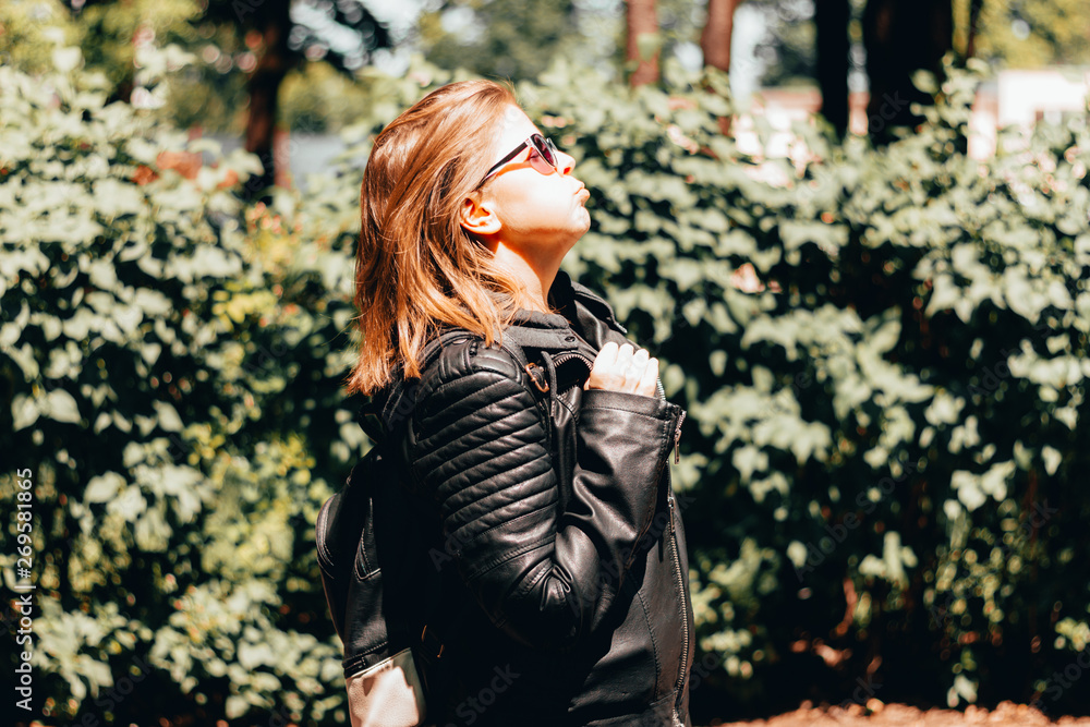 Young woman with brown hair wearing sunglasses and a leather jacket sitting in the bright hot sun – Thirsty and tired girl on a torrid summer day – Concept image for dehydration and overheating Young woman with brown hair wearing sunglasses and a leather jacket sitting in the bright hot sun – Thirsty and tired girl on a torrid summer day – Concept image for dehydration and overheating