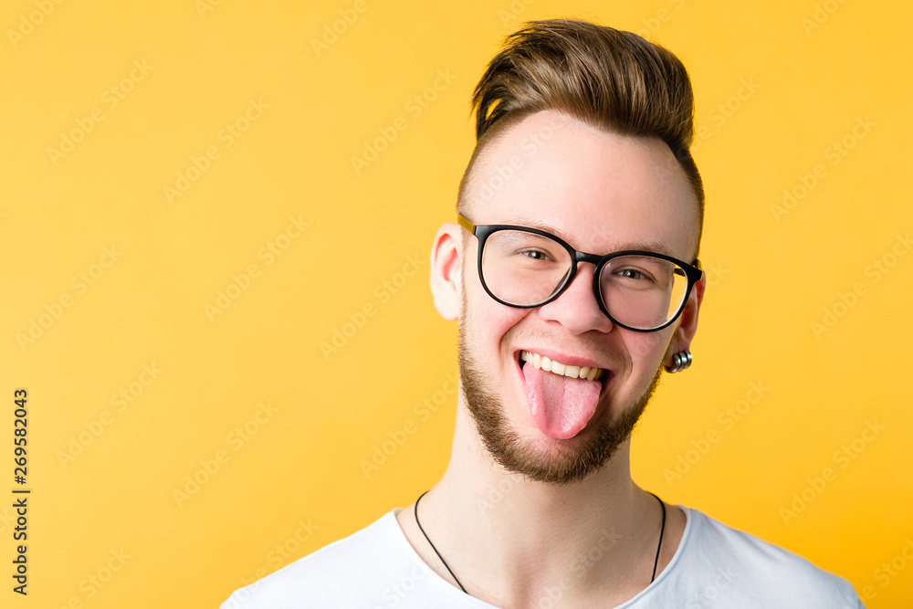 Portrait of positive, cheerful young guy with trendy comb over haircut. Funny emotional man sticking tongue out. Copy space. Portrait of positive, cheerful young guy with trendy comb over haircut. Funny emotional man sticking tongue out. Copy space.