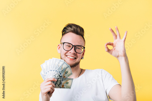 Canvas Print Happy young man bearded hipster holding dollar cash bunch showing ok sign