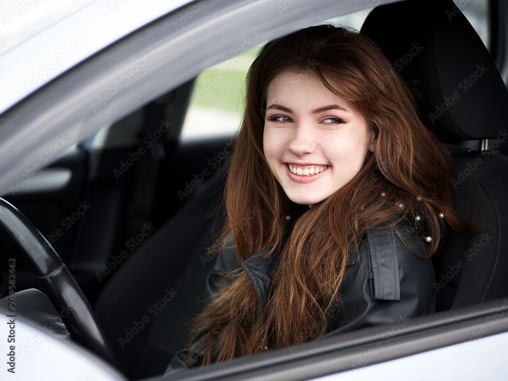 Close up portrait of young attractive red hair self-employed business woman driver sitting in white car stuck in a city traffic jam staring into camera running late to work noonday bleached colors