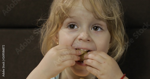 Girl sitting on sofa and eating corn puffs. Child taste puffcorns