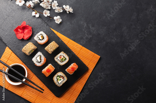 Set of sushi and maki rolls with branch of white flowers on stone table photo