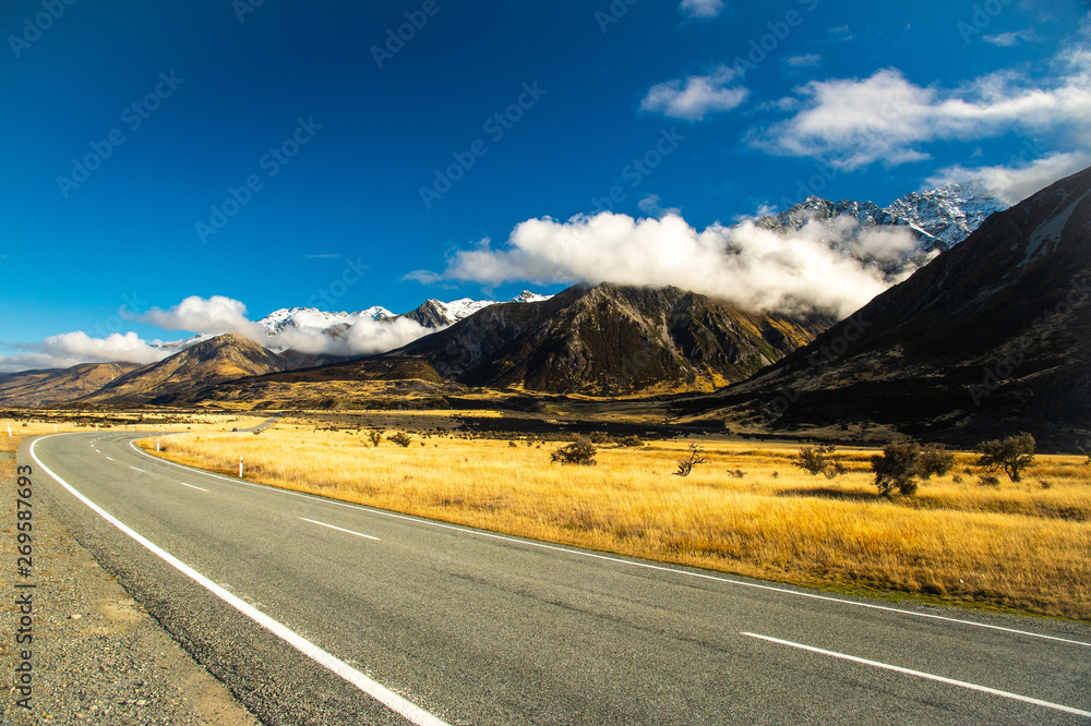Naklejka premium Landscape straight empty highway with blue sky and white clouds on the way to Aoraki Mount Cook National Park, New Zealand.