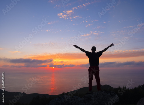 man doing sports with raised arms in front of blue sky and sunset over the sea, Euskadi