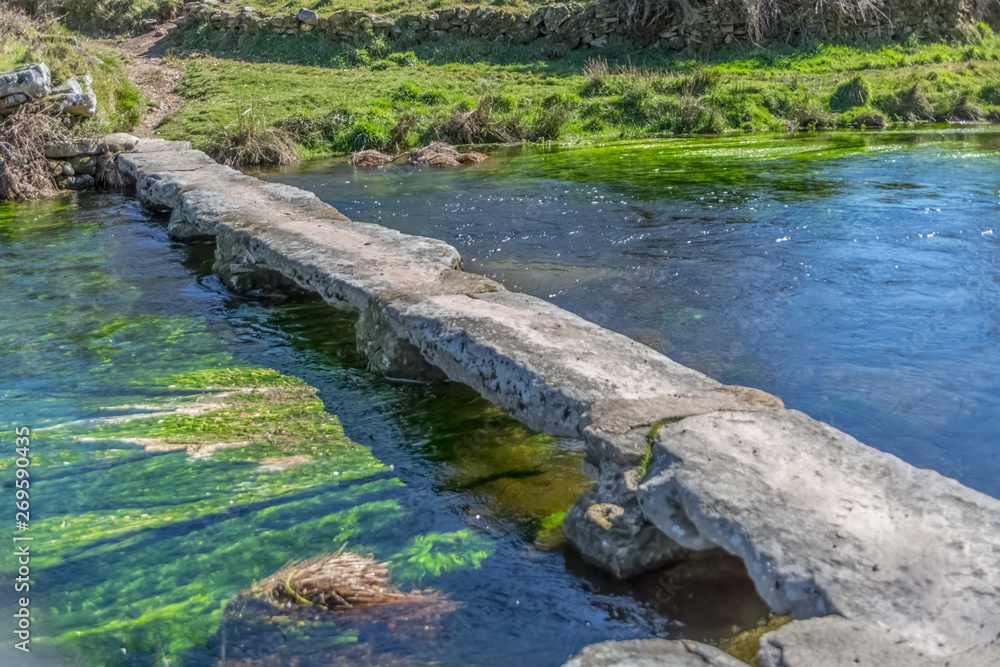 View of a river, with old and archaic stone bridge for pedestrian passage View of a river, with old and archaic stone bridge for pedestrian passage
