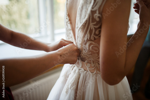 hands of girlfriends button the dress of the bride