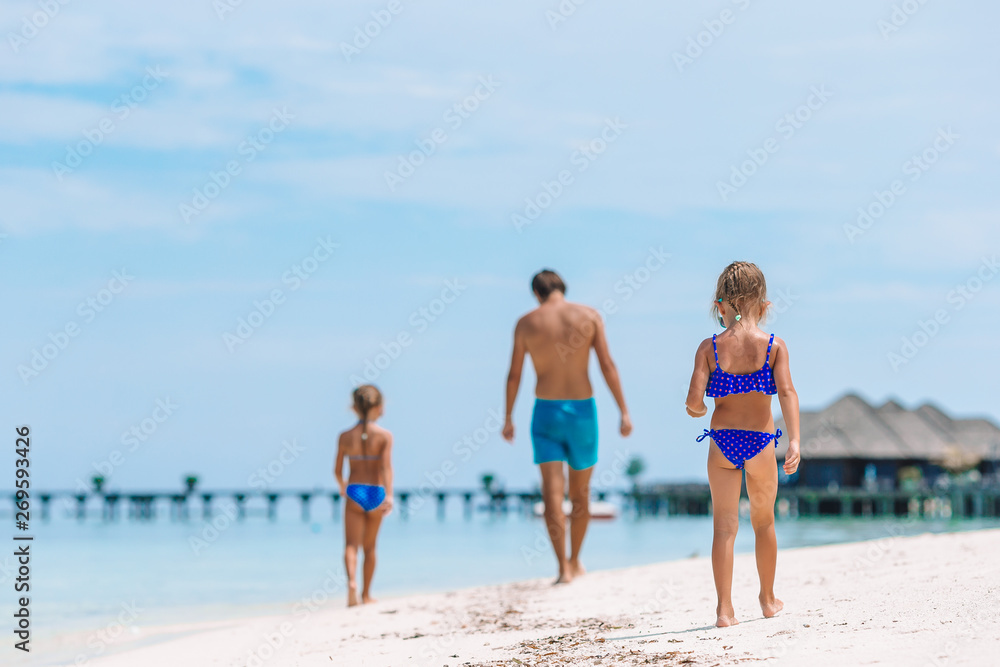 Happy father and his adorable little daughters at tropical beach having fun