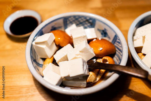 Traditional japanese ceramic bowl in restaurant with wooden table and spring vegetable dish with honey mushrooms and cubed tofu with soy sauce photo