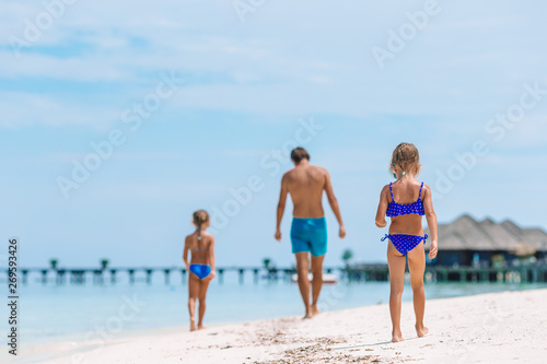 Happy father and his adorable little daughters at tropical beach having fun