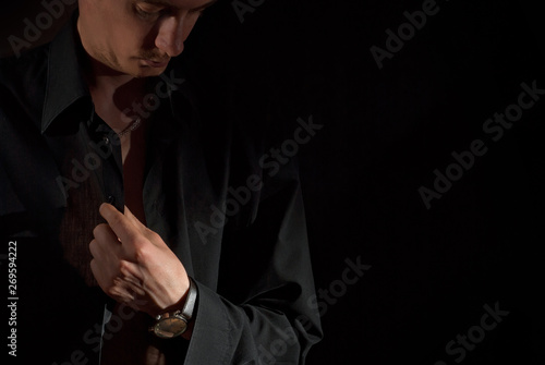 A man wears a dark shirt on a naked body. Isolate with copy space on black background. The guy hooks up the buttons.