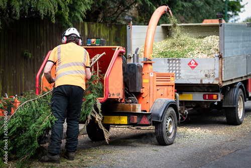 Male Arborist using a working wood chipper machine.The tree surgeon is wearing a safety helmet with a visor and ear protectors. photo