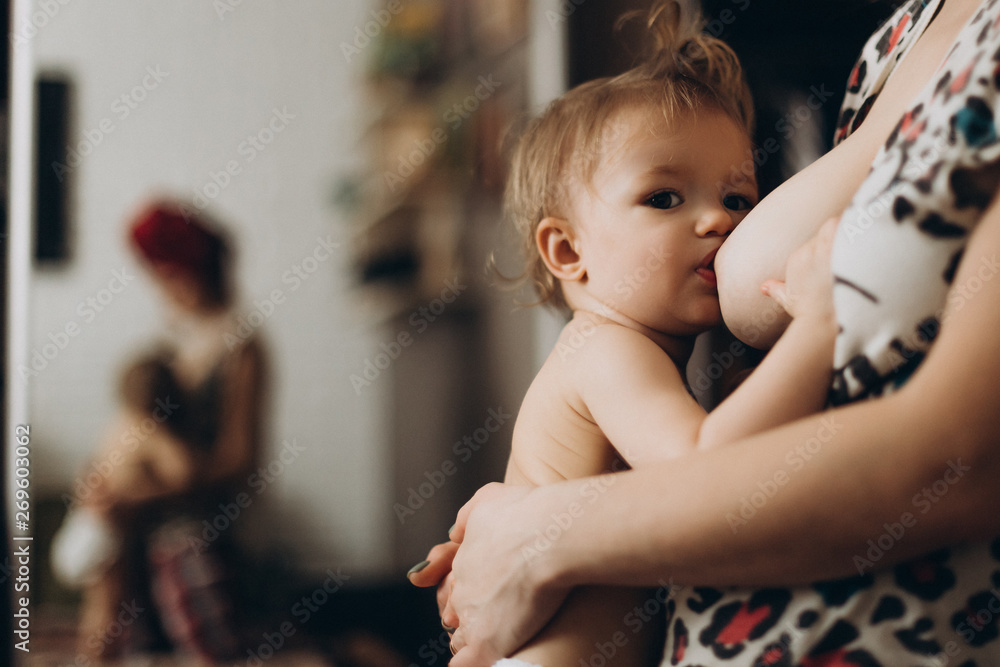 Young beautiful woman is breastfeeding a little baby in a cozy room in home Young beautiful woman is breastfeeding a little baby in a cozy room in home