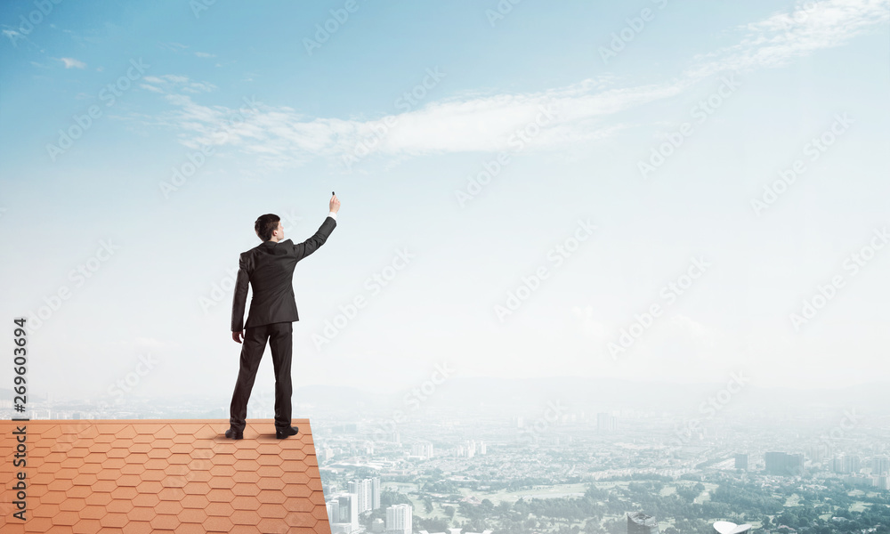 Businessman on house roof touch empty space. Mixed media Businessman on house roof touch empty space. Mixed media