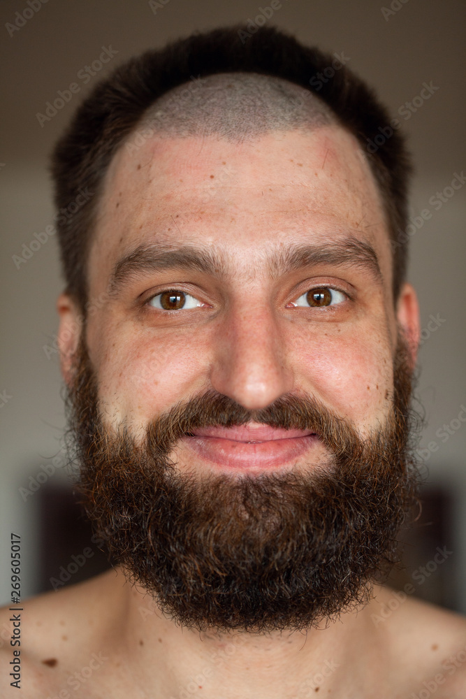 Obraz premium Portrait of man with an unusual hairstyle and beard with a naked torso, looks into the camera 
