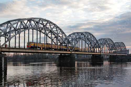 Fototapeta Naklejka Na Ścianę i Meble -  The train travels along the railway bridge across the Daugava river