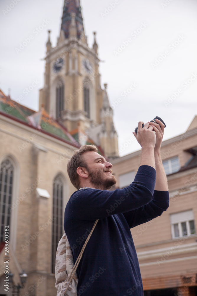 One young man, tourist or traveler using a DSLR camera, in a old European style architecture city behind.