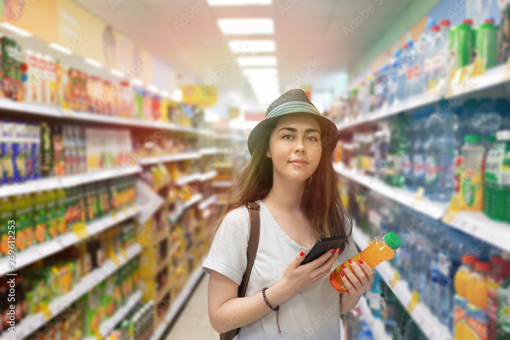 Young beautiful woman chooses a bottle of juice in the supermarket and checks the QR code on the label. The concept of modern technology and shopping in the store. Light