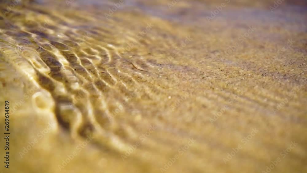 Macro shot of water trickling in on a sandy beach and then flowing back out into the body of water Macro shot of water trickling in on a sandy beach and then flowing back out into the body of water