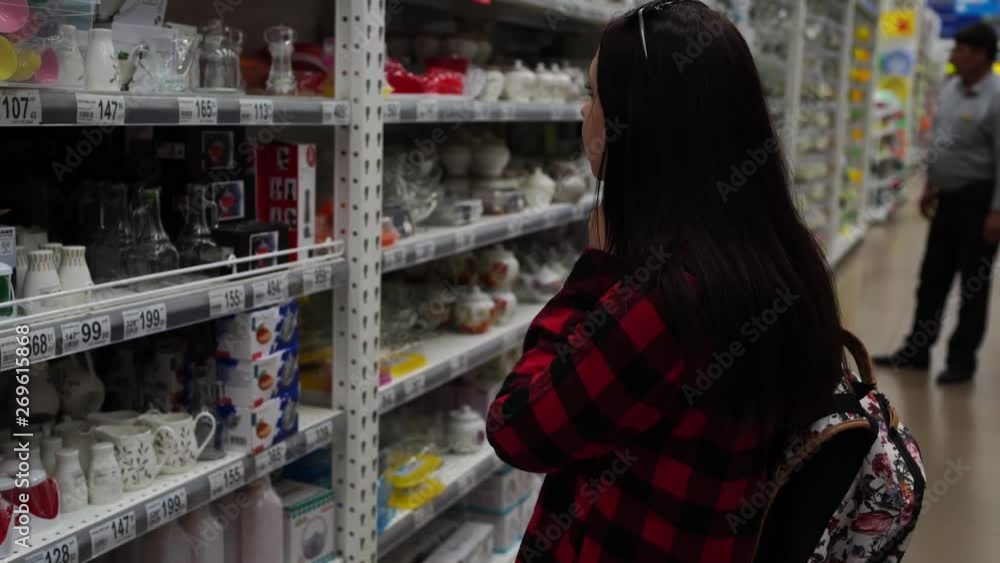 Housewife buys dishes for the kitchen. A woman buys dishes in the store, examines various items of dishes. Housewife buys dishes for the kitchen. A woman buys dishes in the store, examines various items of dishes.