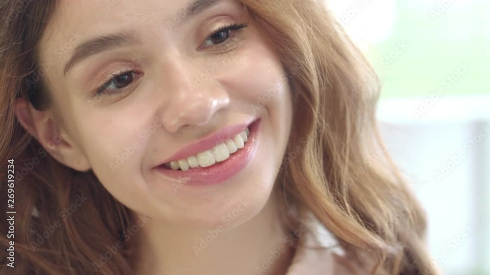 Cheerful woman smiling and looking to face mirror in home bathroom