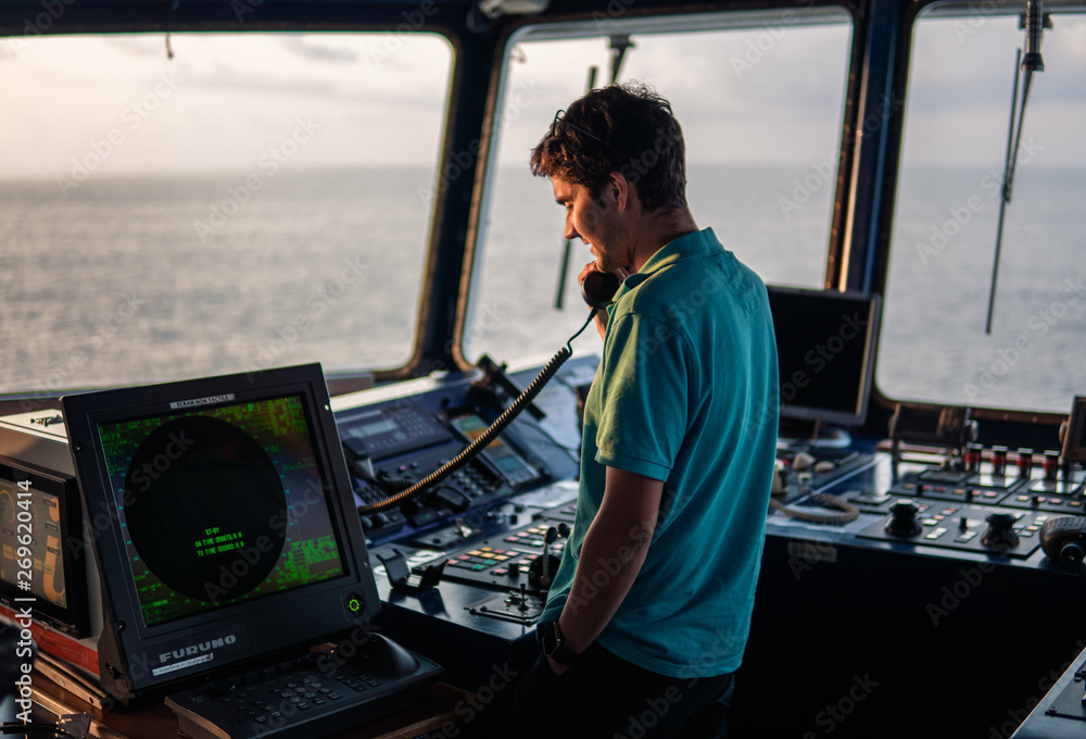 Marine navigational officer is reporting by VHF radio during navigation watch. Bridge GMDSS watch Marine navigational officer is reporting by VHF radio during navigation watch. Bridge GMDSS watch