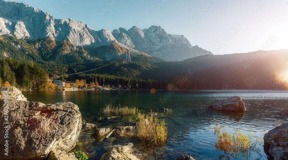 Awesome alpine highlands in sunny day. Nature Landscape. The Eibsee Lake in front of the Zugspitze under sunlight reflected in water. Majestic Autumn Scenery. Eibsee, Bavaria Germany.
