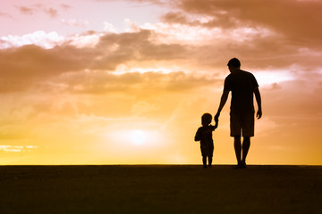 Silhouette of loving father walking side by side with son holding hands. 
