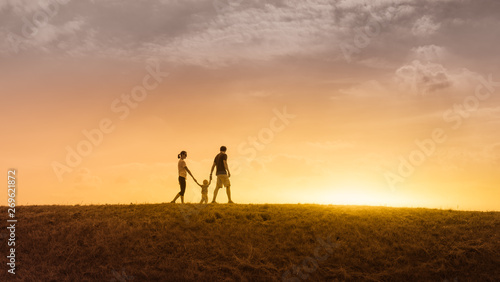 happy family of three holding hands walking together in a grass field at sunset