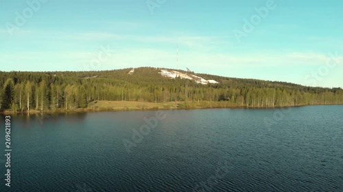 Aerial, reverse, drone shot, above lake Sarkinen, away from Vuokatinvaara hills, on a sunny, spring day, in Vuokatti, Sotkamo, Kainuu, Finland photo