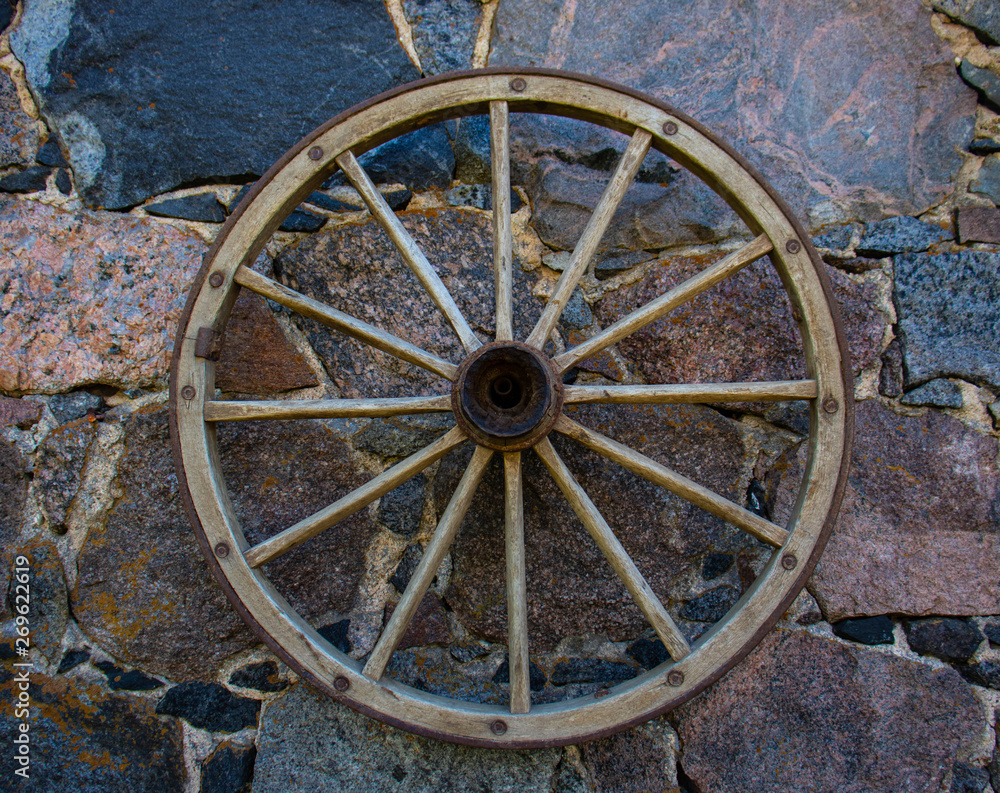 An old cartwheel hangs on a wall of multi-colored stones.