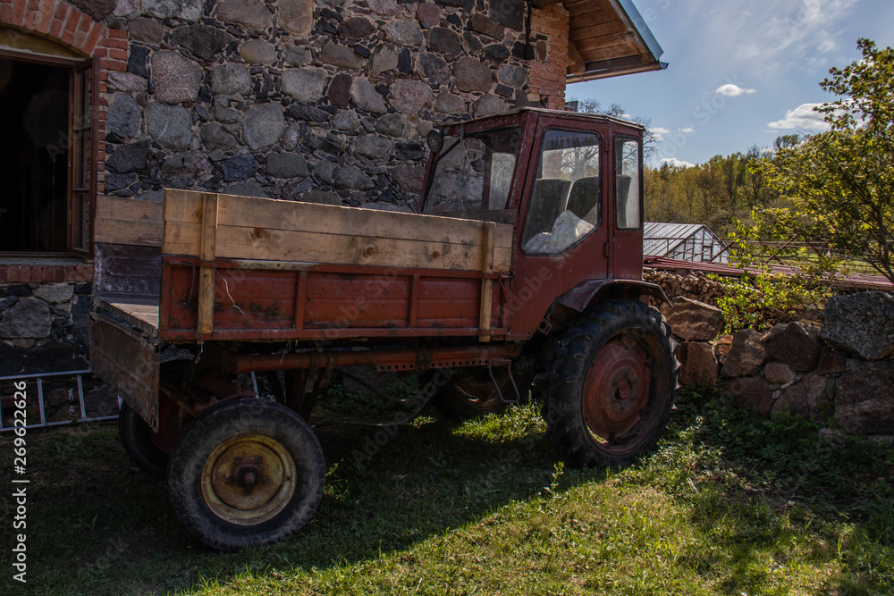 Obraz premium Old red tractor stands near the house with a stone wall