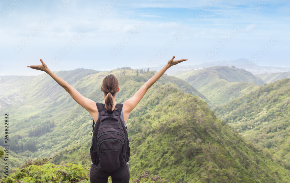 young woman hiker with open arms raised in the mountains