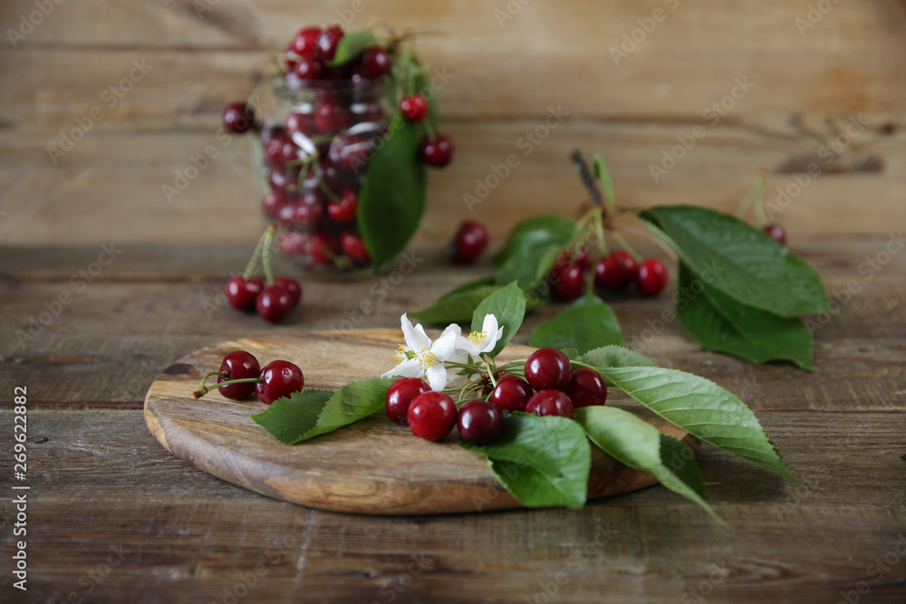 fresh organic sweet cherries in the glass jar with a branch of sweet cherries on the wooden rustic background. Healthy food concept. With copy space for text. Closeup. 