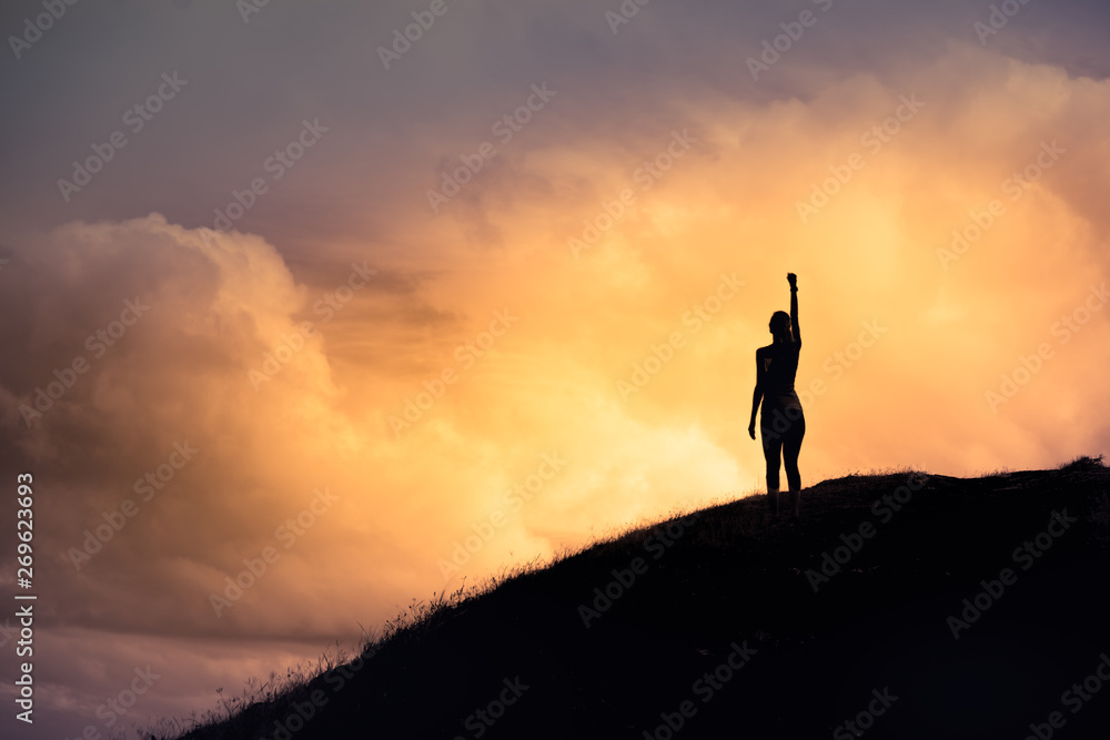Strong woman with fist in the air standing on top a mountain. Triumph, victory and feeling determined.