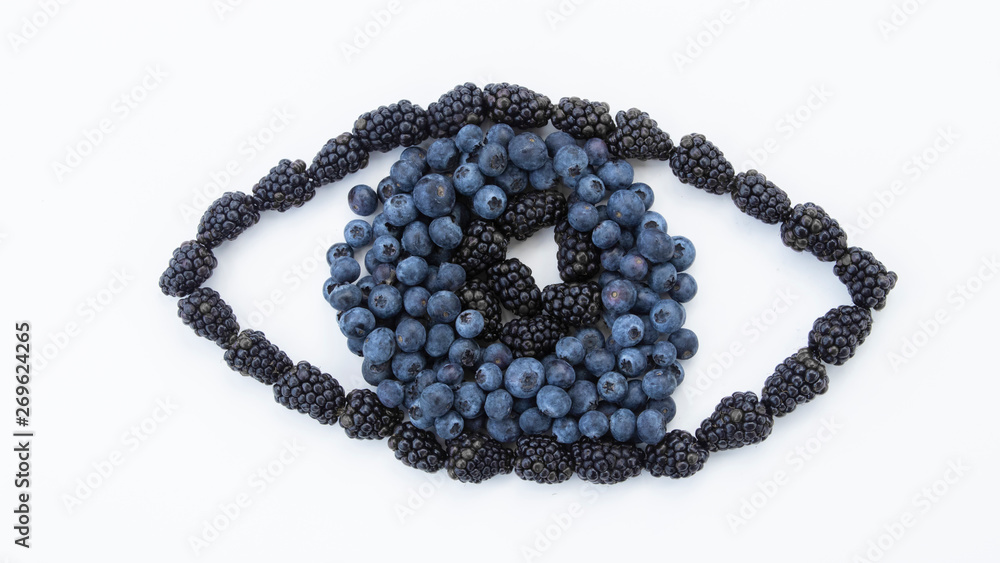 An eye created out of fresh fruit. Resting on a white background with a gleam in the pupil made with blackberries surrounded by fresh blueberries shaping the iris on a white background. An eye created out of fresh fruit. Resting on a white background with a gleam in the pupil made with blackberries surrounded by fresh blueberries shaping the iris on a white background.