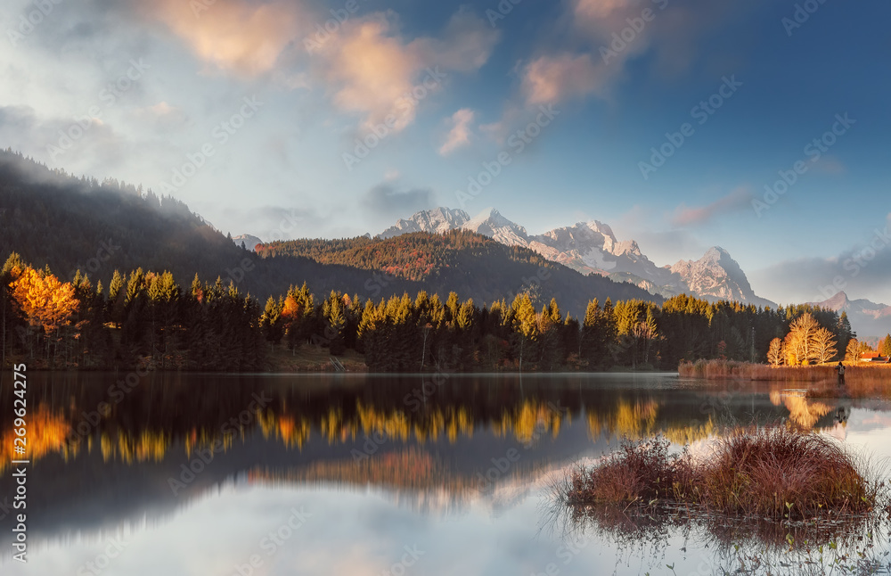 fantastic foggy landscape at Germanian Alps. Colrful Clouds on the Blue Sky over the Zugspitze mountains at early morning in autumn, Bavaria, Germany. Fresh grass on foreground.