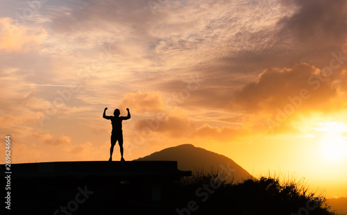 People, power, strength, and determination. Strong man flexing his muscles against sunset. 