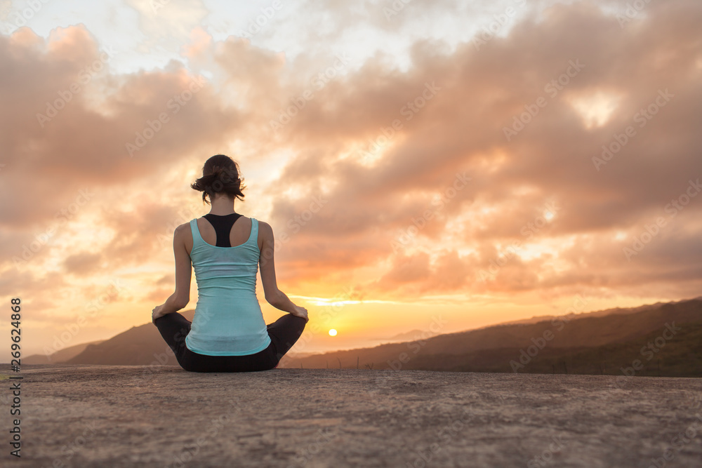 young woman practicing yoga on mountain top at sunset 