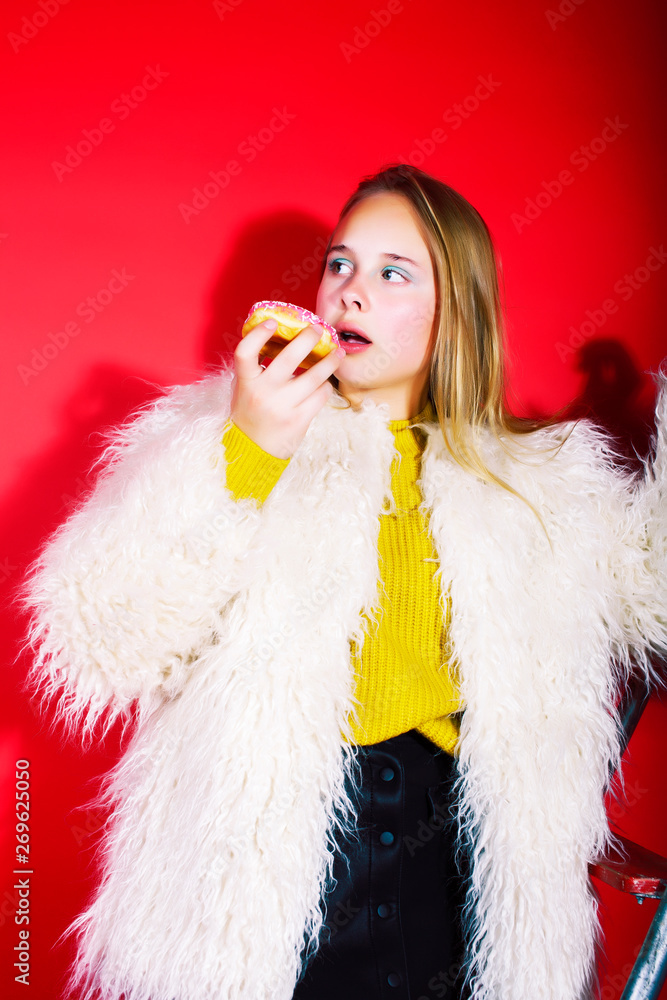 little cute blond teenage girl posing in fashion style with donut on red background, lifestyle people concept little cute blond teenage girl posing in fashion style with donut on red background, lifestyle people concept