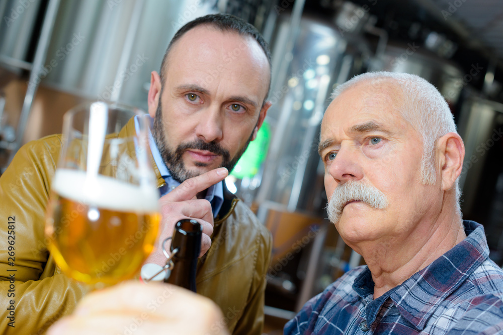 two mature men examining glass of lager in brewery two mature men examining glass of lager in brewery