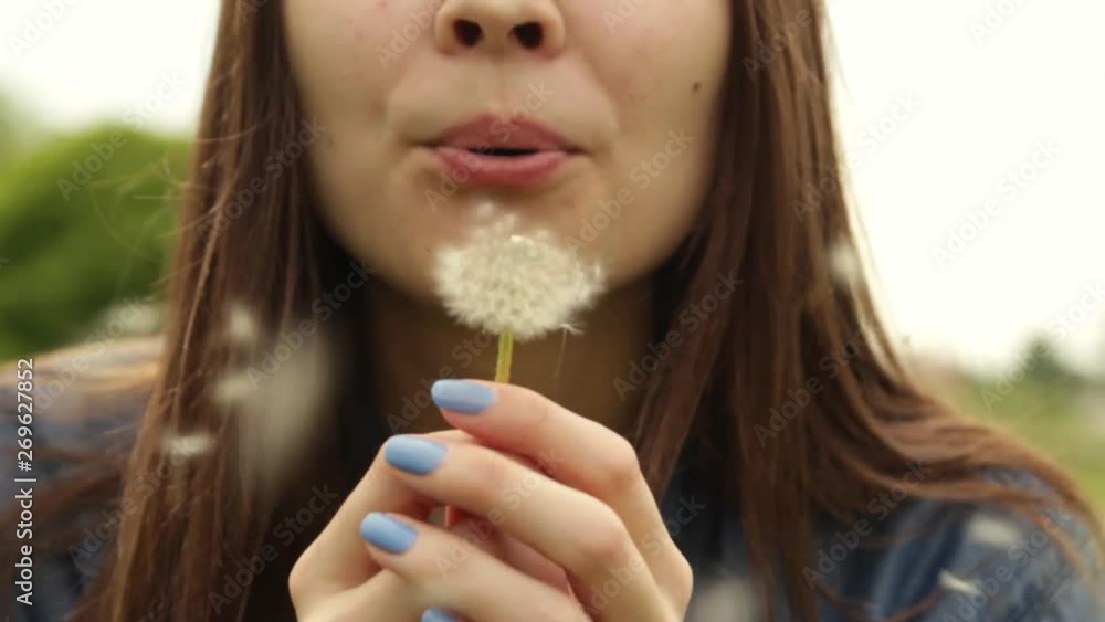 Unrecognizable joyful woman blowing on dandelion and smiling while standing in green park Unrecognizable joyful woman blowing on dandelion and smiling while standing in green park