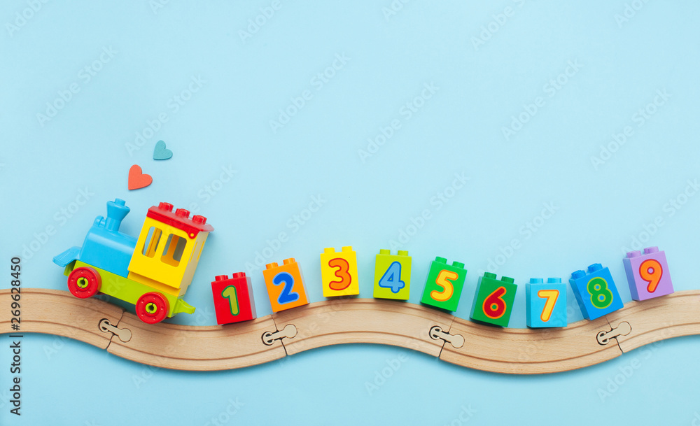 Kids toy train with numbers on toy wooden railway on light blue background with copy space - obrazy, fototapety, plakaty 