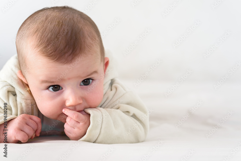 Portrait of an adorable smiling baby biting her own fingers putting her fist in her mouth. Portrait of an adorable smiling baby biting her own fingers putting her fist in her mouth.