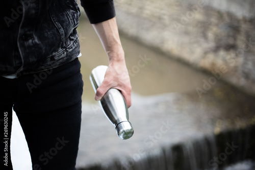 Close-up of man hand holding steel bottle for water, on river background
